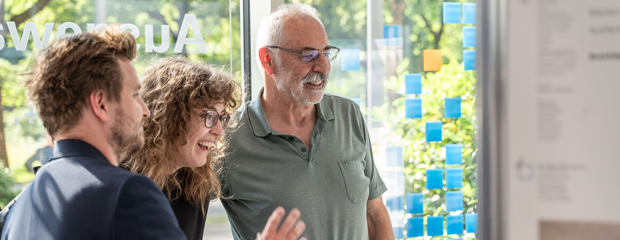 Drei Personen betrachten eine Tafel in einer Ausstellung
