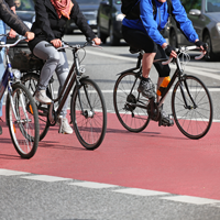 Ein roter Radwegstreifen mit drei Radfahrern, die nur ausschnittsweise zu sehen sind, die Köpfe sind oben abgeschnitten