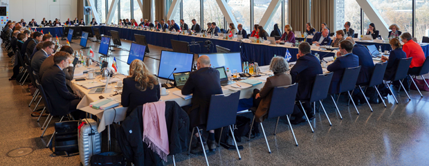 Im Rechteck angeordnete Konferenztische mit Personen, die dort sitzen und arbeiten
