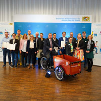 Gruppenfoto von Bayerns Verkehrsminister Christian Bernreiter mit Vertreterinnen und Vertretern der Modellkommunen. Der Minister sitzt auf einem Lastenrad.