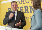 Staatsminister Christian Bernreiter im Gespräch mit Moderatorin Franziska Troger über die Geschichte und aktuelle Herausforderungen im Hochbau in Bayern.